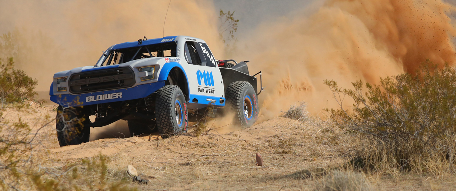 Blower Motorsports truck with cloud of dust behind it racing in the desert